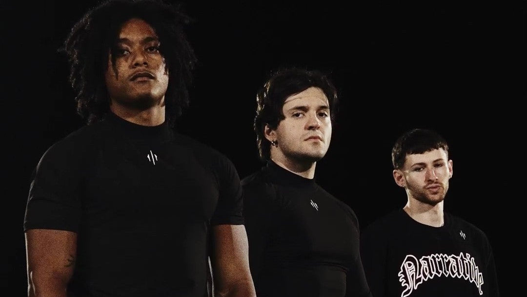 Three individuals in black outfits standing on a sports field with a dark background