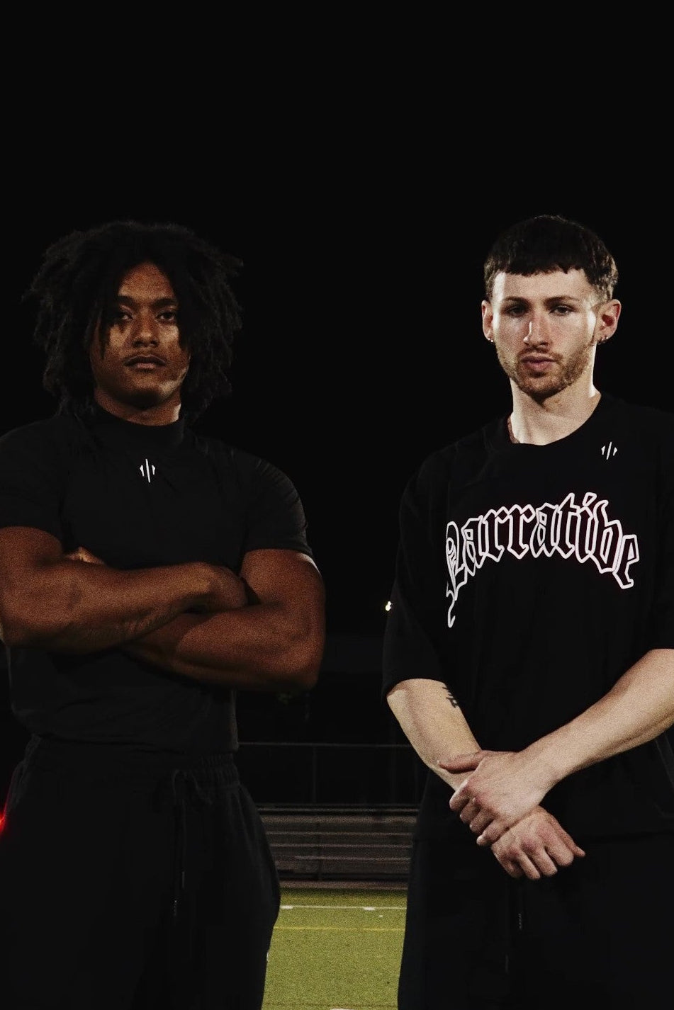 Two men standing on a sports field wearing black Narrative Mesh t-shirts with visible branding.